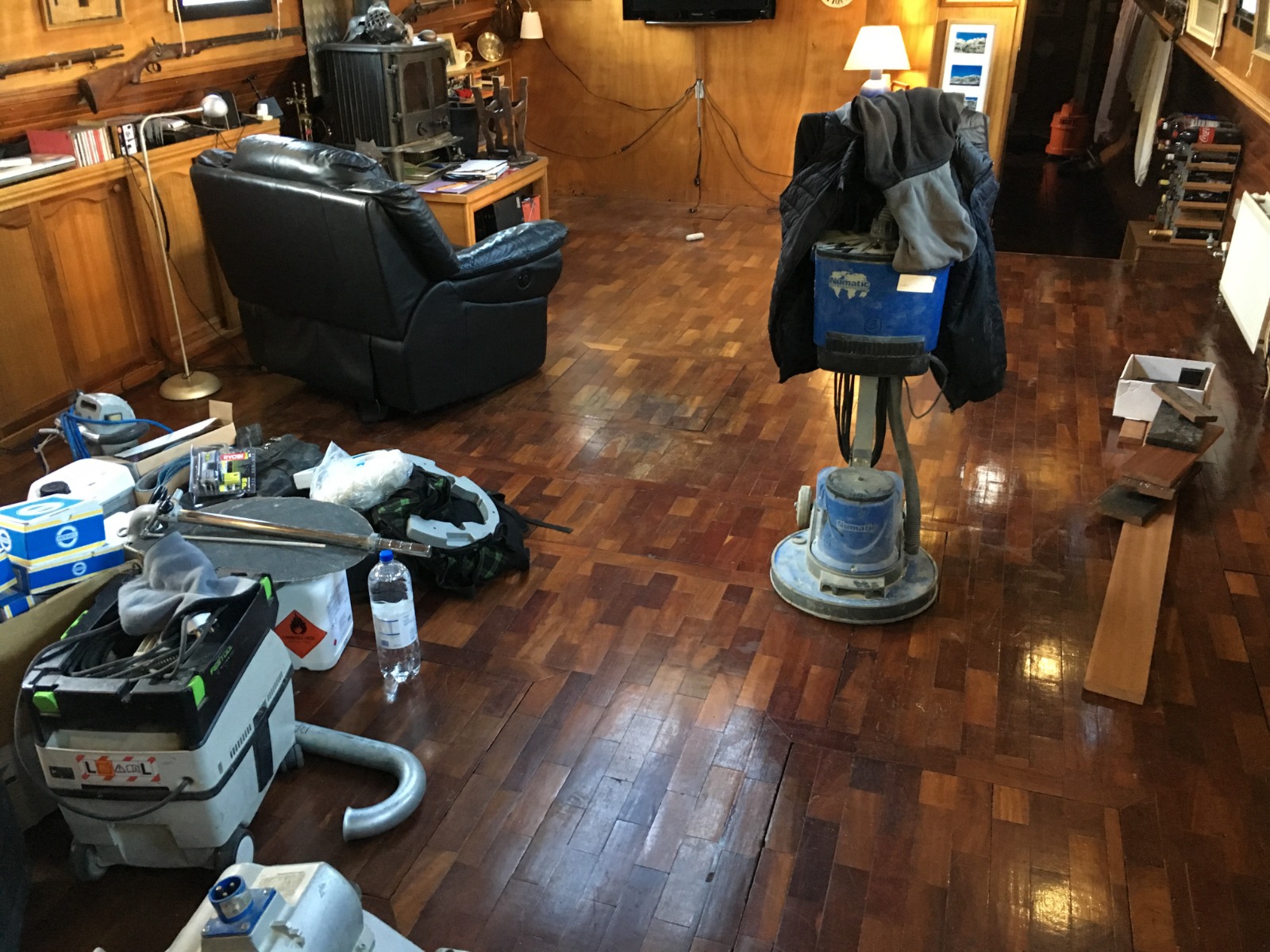 Commercial Floor Sanding in Stamford Hill on a dark hardwood parquet block floor, with sanding machines and tools set up in a wood-panelled commercial lounge area.