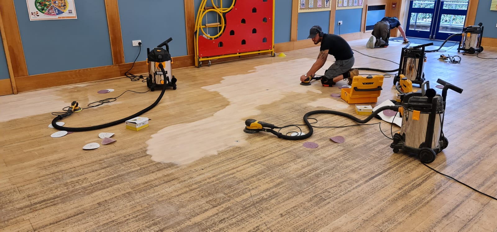 Commercial Floor Sanding in Stamford Hill underway in a school hall, with technicians using dust-free sanding machines on a worn maple hardwood floor to restore the surface.