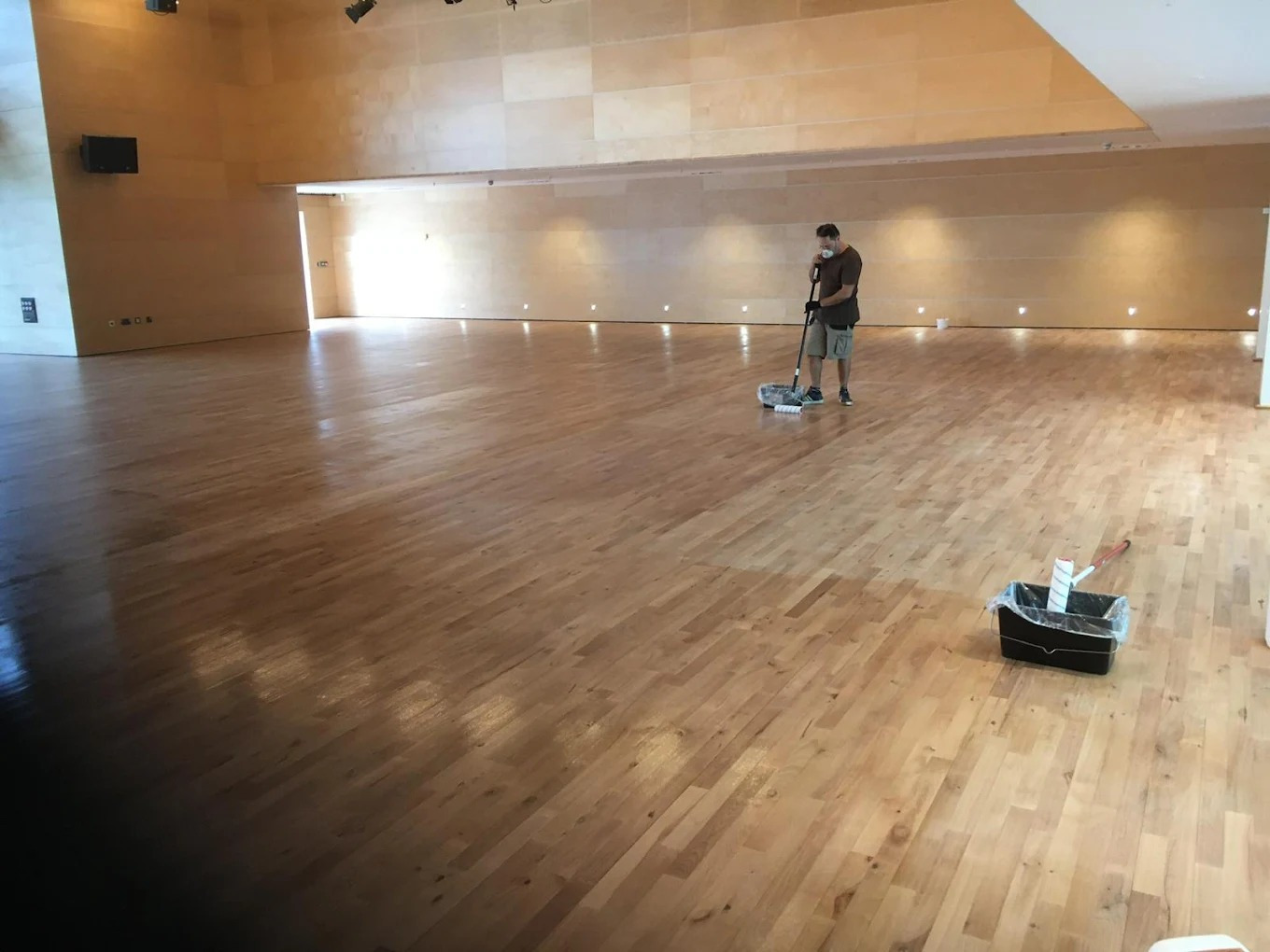 Technician applying lacquer after Commercial Floor Sanding in a large Stamford Hill hall with a smooth maple strip hardwood floor.