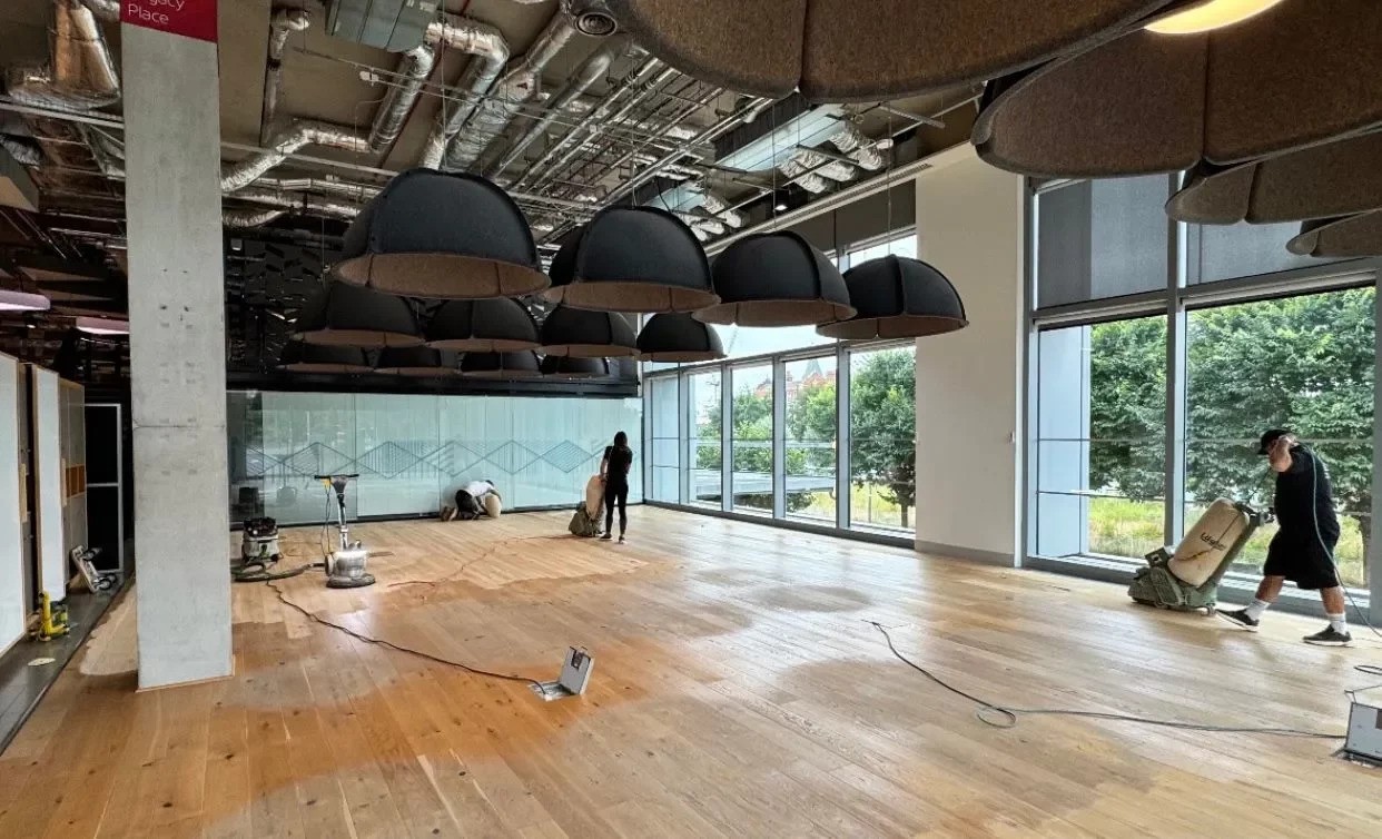Commercial Floor Sanding in Stamford Hill inside a modern office, with technicians sanding a large oak plank hardwood floor to restore a smooth, even finish.